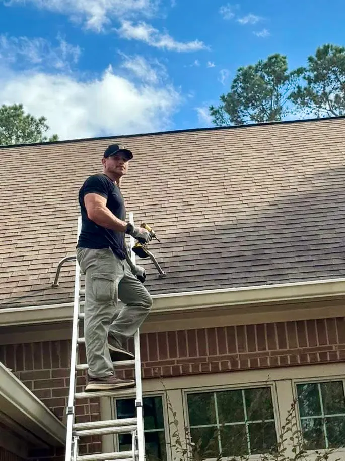 Josh Beken working from a ladder along a home's gutter line