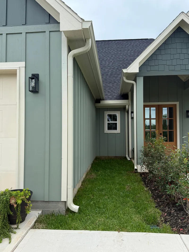 Close view of white gutters and downspouts running along a green board-and-batten home